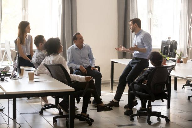 Male team leader boss talking to diverse business people at office meeting, multiracial employees group listening to ceo mentor coach speaking explaining new idea at corporate training or briefing