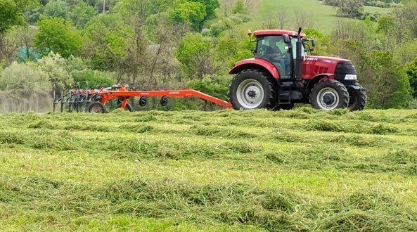 Red tractor cutting hay in grassy field